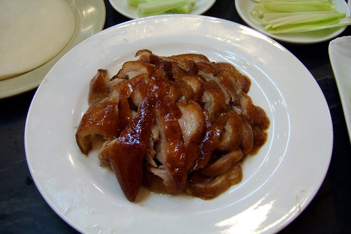 Sliced Peking duck with glossy lacquered skin served on a white plate with cucumber strips and pancakes