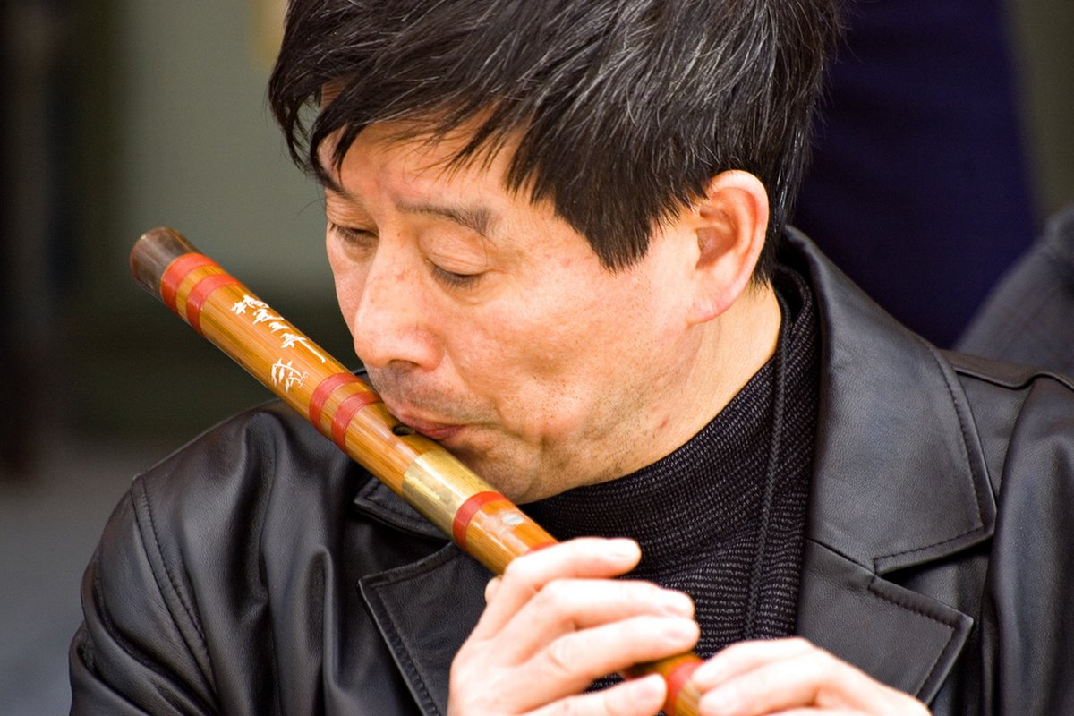 A Chinese musician playing the dizi — the traditional bamboo transverse flute — with eyes closed in concentration