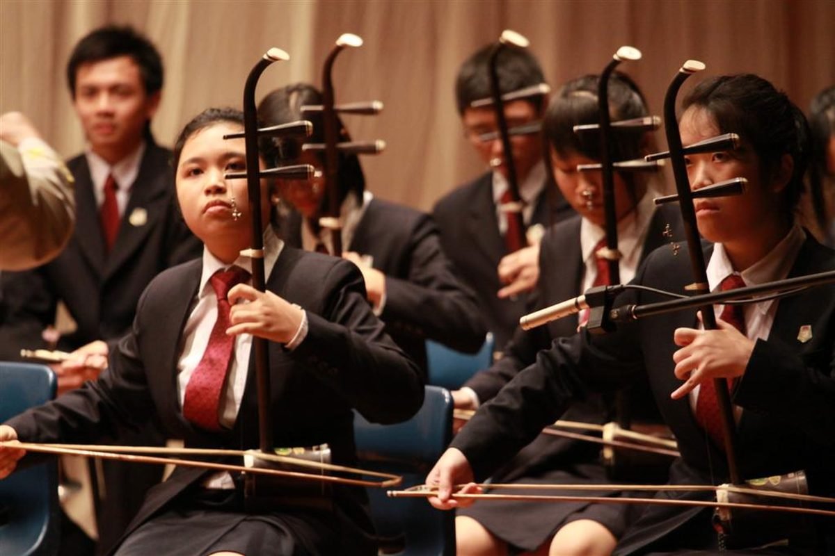 Multiple erhu players performing in a Chinese orchestra, each holding the two-stringed fiddle upright with horsehair bows