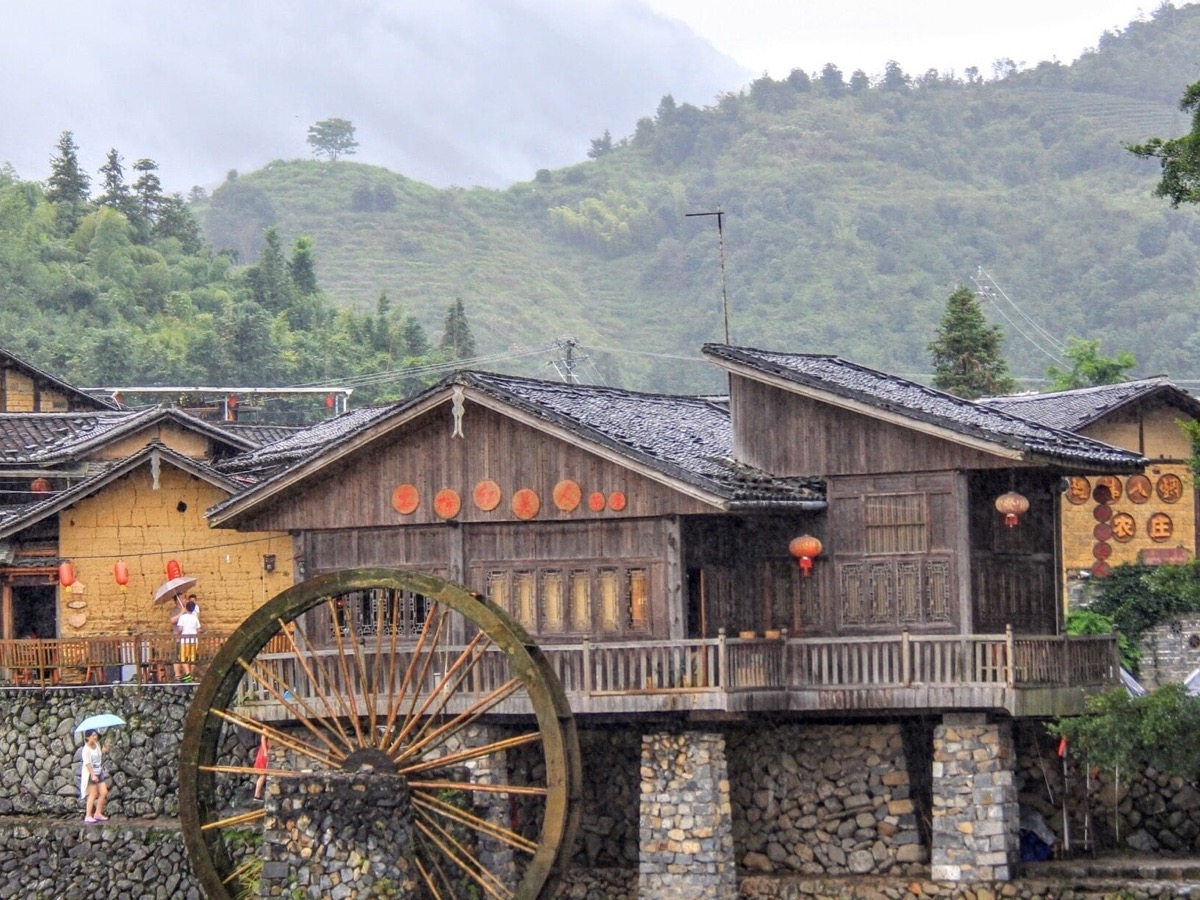 Traditional Sanming village in inland Fujian — wooden buildings, water wheel and red lanterns along a misty river