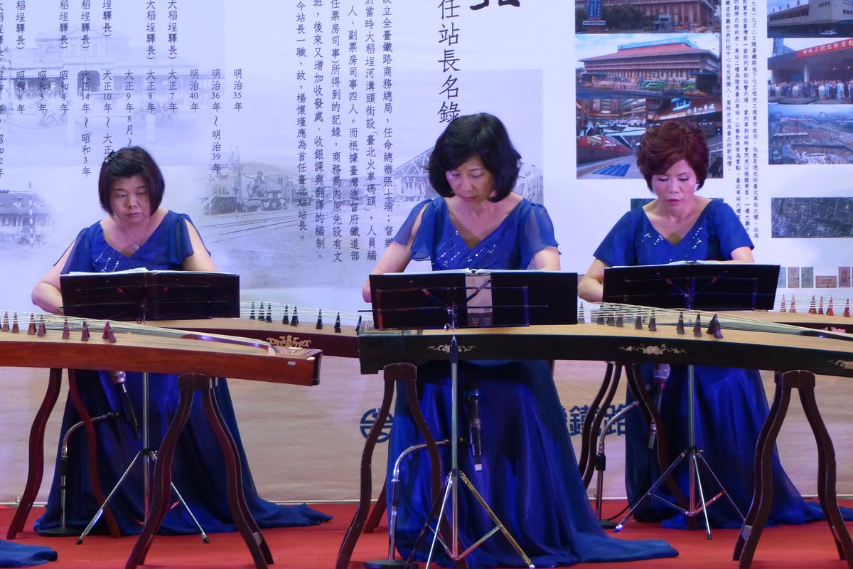 Three women performing on guzheng — the traditional Chinese plucked zither — at a formal stage concert