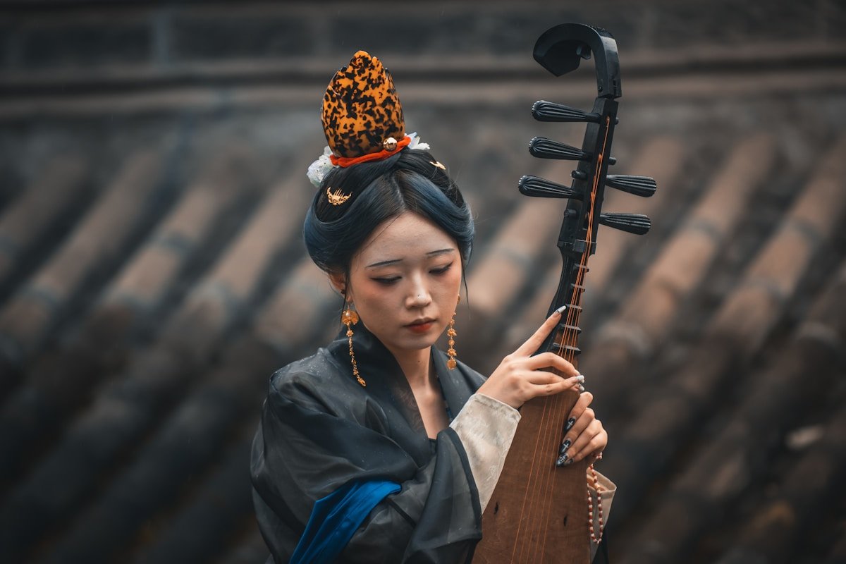 A woman in traditional Chinese costume playing the pipa lute in a courtyard setting