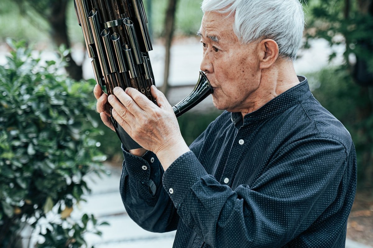 An elderly Chinese musician playing the sheng — the traditional free-reed mouth organ with bamboo pipes