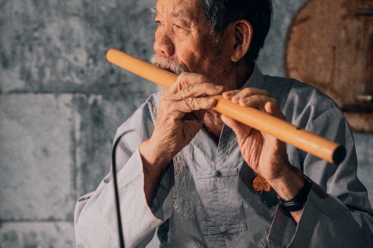 An elderly Chinese musician playing the xiao — the traditional vertical end-blown bamboo flute