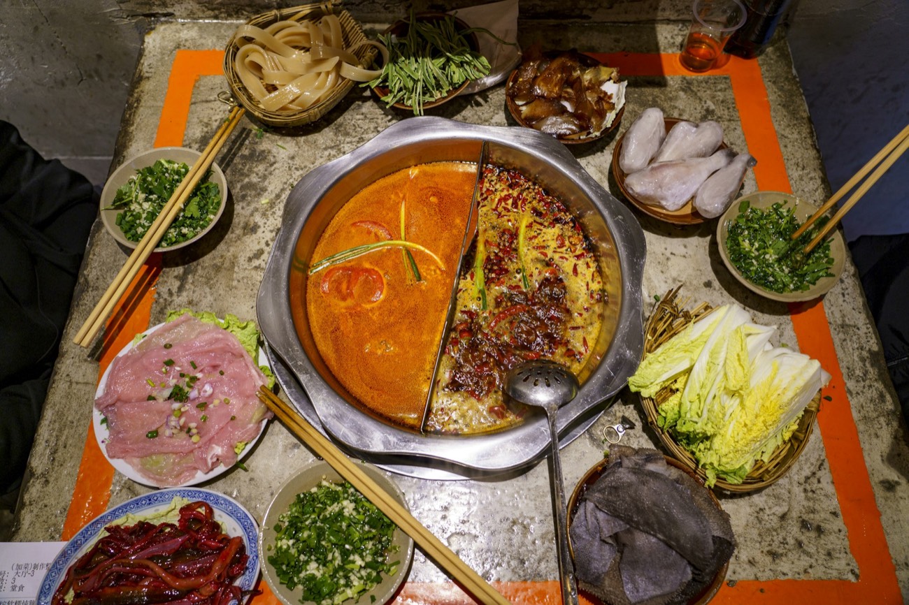A bubbling Chongqing málà hotpot surrounded by dishes ready to cook