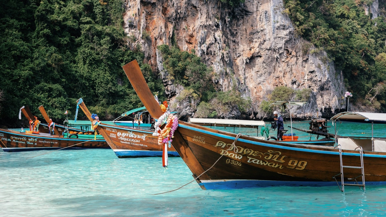 Traditional long-tail boats moored in turquoise water below limestone karst cliffs near Phuket — learn Mandarin online from Phuket
