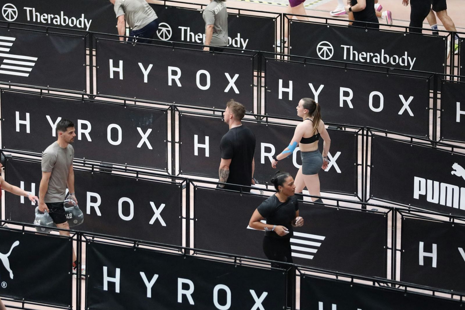 Competitors walking past a wall of Hyrox and sponsor branding at a race venue