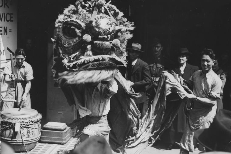 A Chinese lion dancer from Bendigo in Elizabeth Street, Melbourne, around 1943, watched by smiling onlookers outside the Seamen's Union.