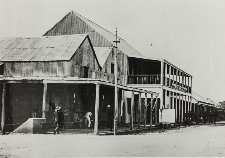 Cavenagh Street, Darwin, in 1915: a two-storey timber store with a balcony and the sign Man Fong Lau, a corrugated-iron store beside it, a man carrying a shoulder pole, and a horse and cart.