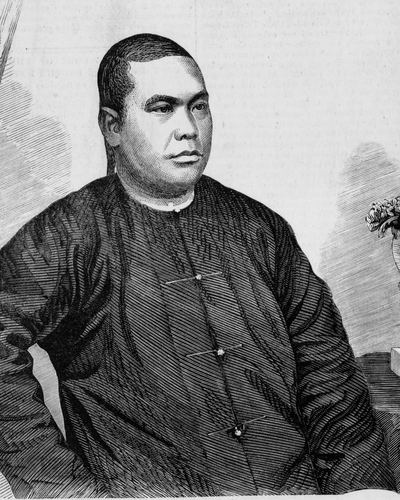 A wood engraving of Lowe Kong Meng in 1866, seated in a dark buttoned jacket beside a vase of flowers.