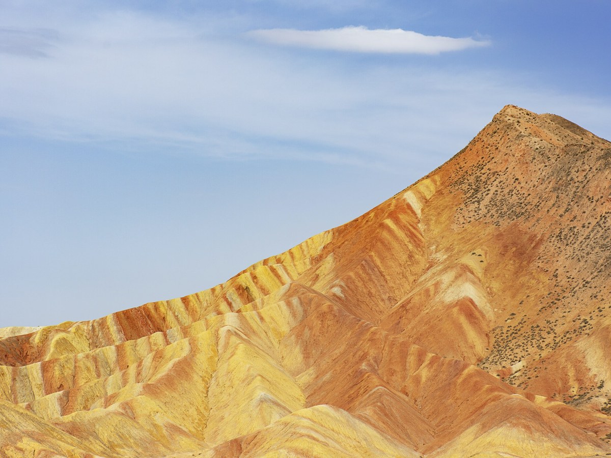 Zhangye Danxia rainbow mountain peak with vivid yellow, orange and red striated layers under a blue sky, Gansu