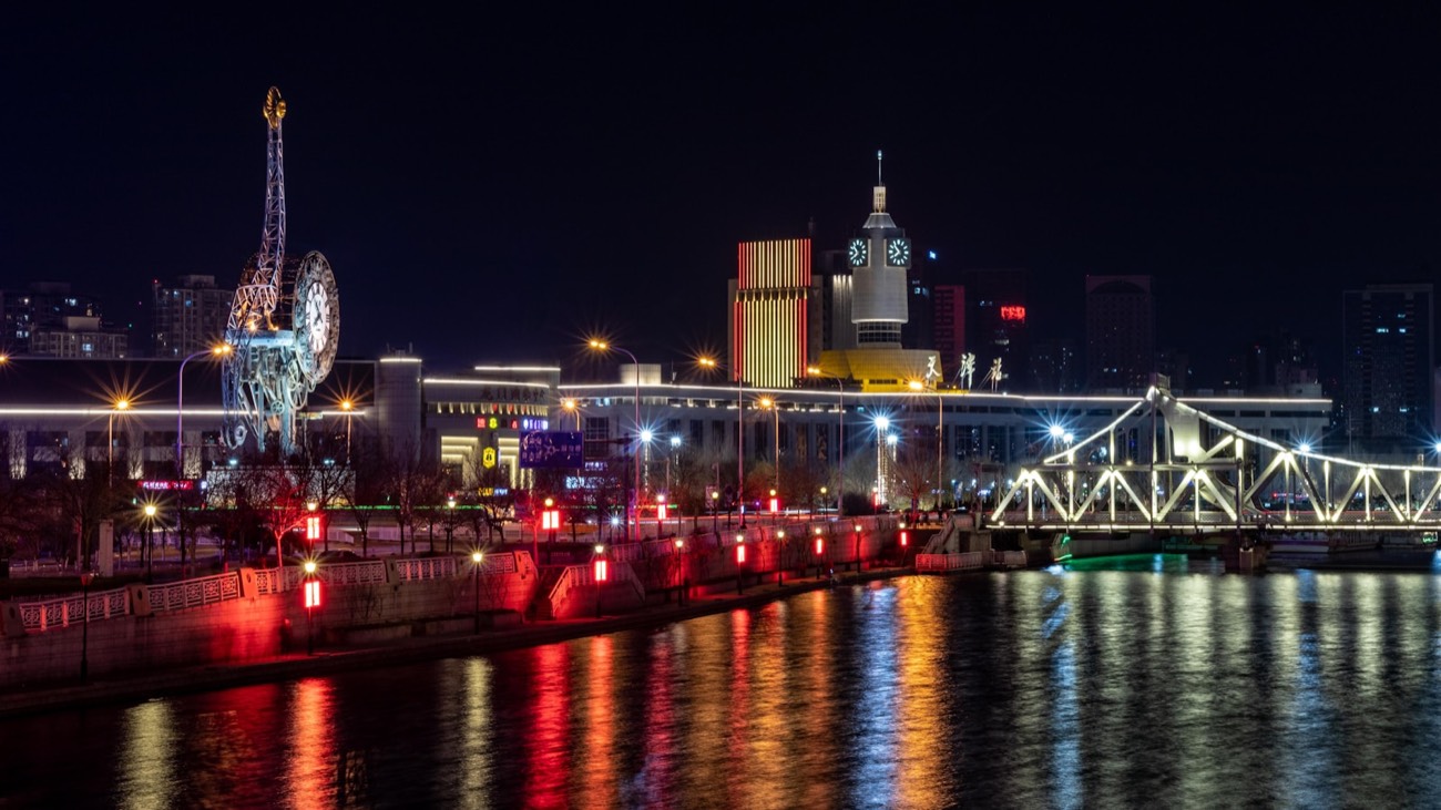The Hai River in Tianjin at night, lined with historic European-era buildings and a steel bridge