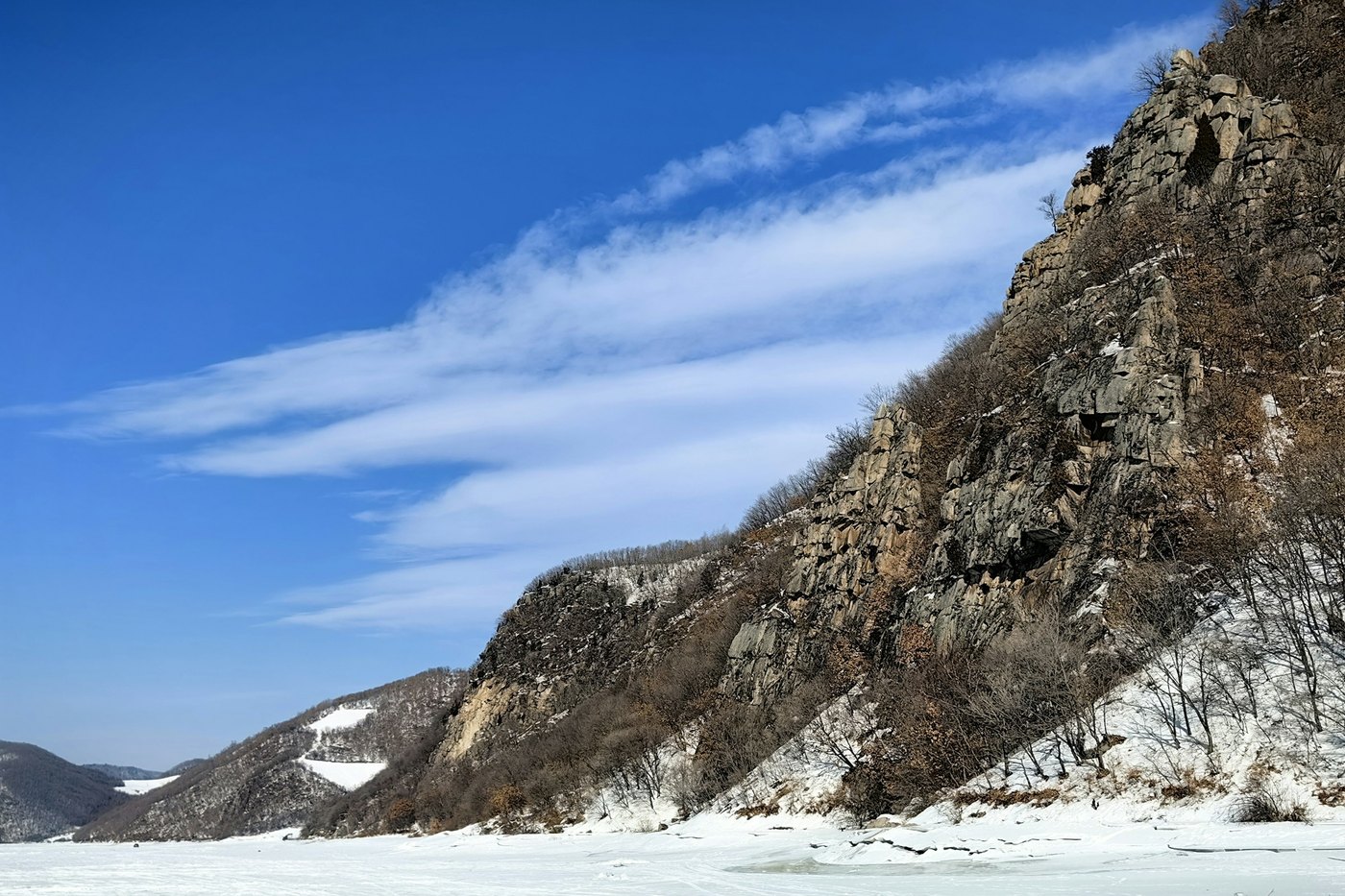 A frozen river below a rocky escarpment in winter near Mudanjiang, Heilongjiang