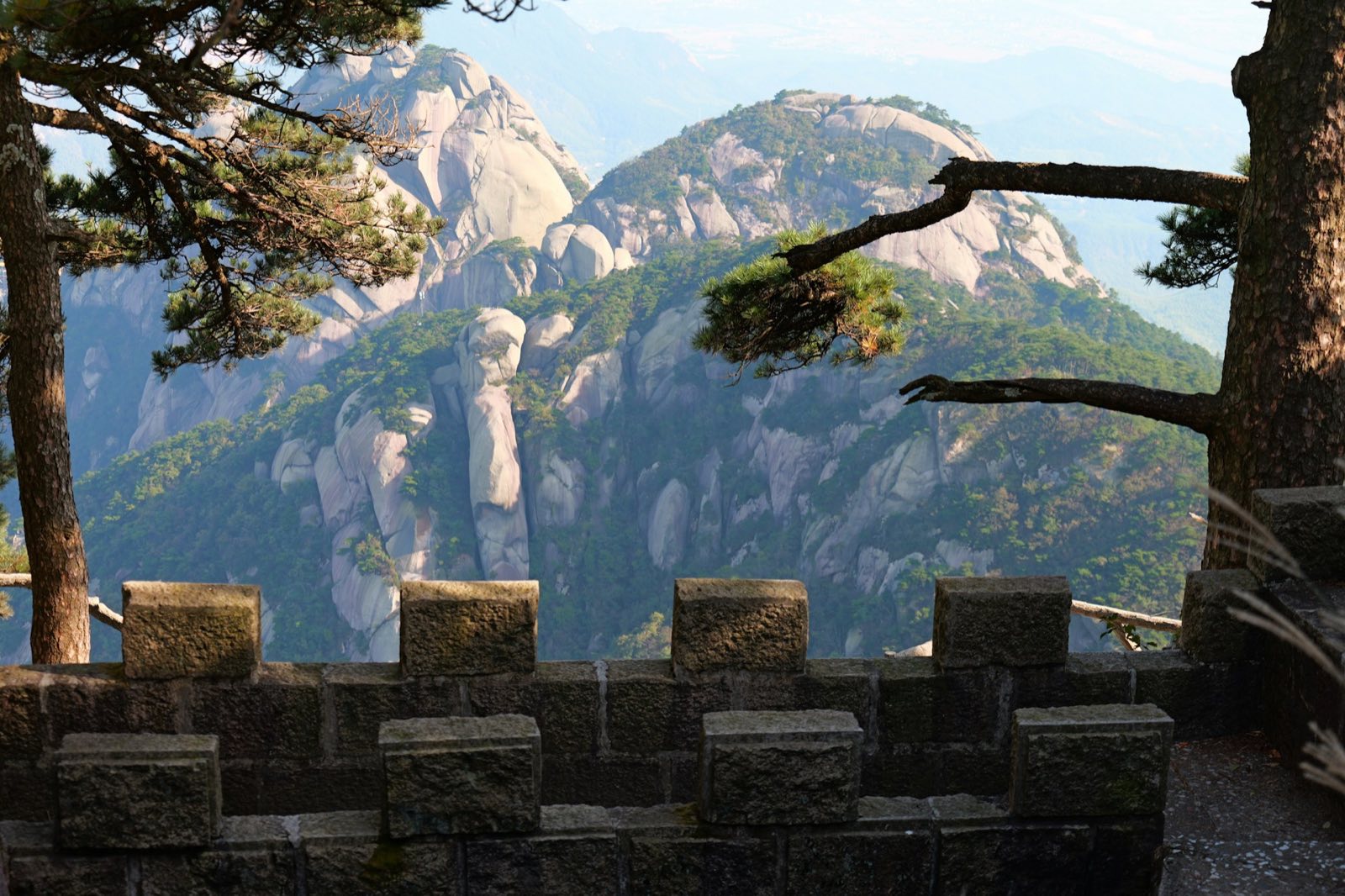 Granite peaks and pine trees in the mountains near Anqing, seen over a stone wall